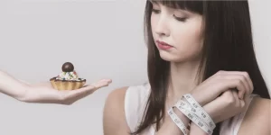 Uma mulher com as mãos amarradas com uma fita métrica. Ela quer comer o doce que está sendo oferecido. Dieta não é eficaz contra a obesidade.
