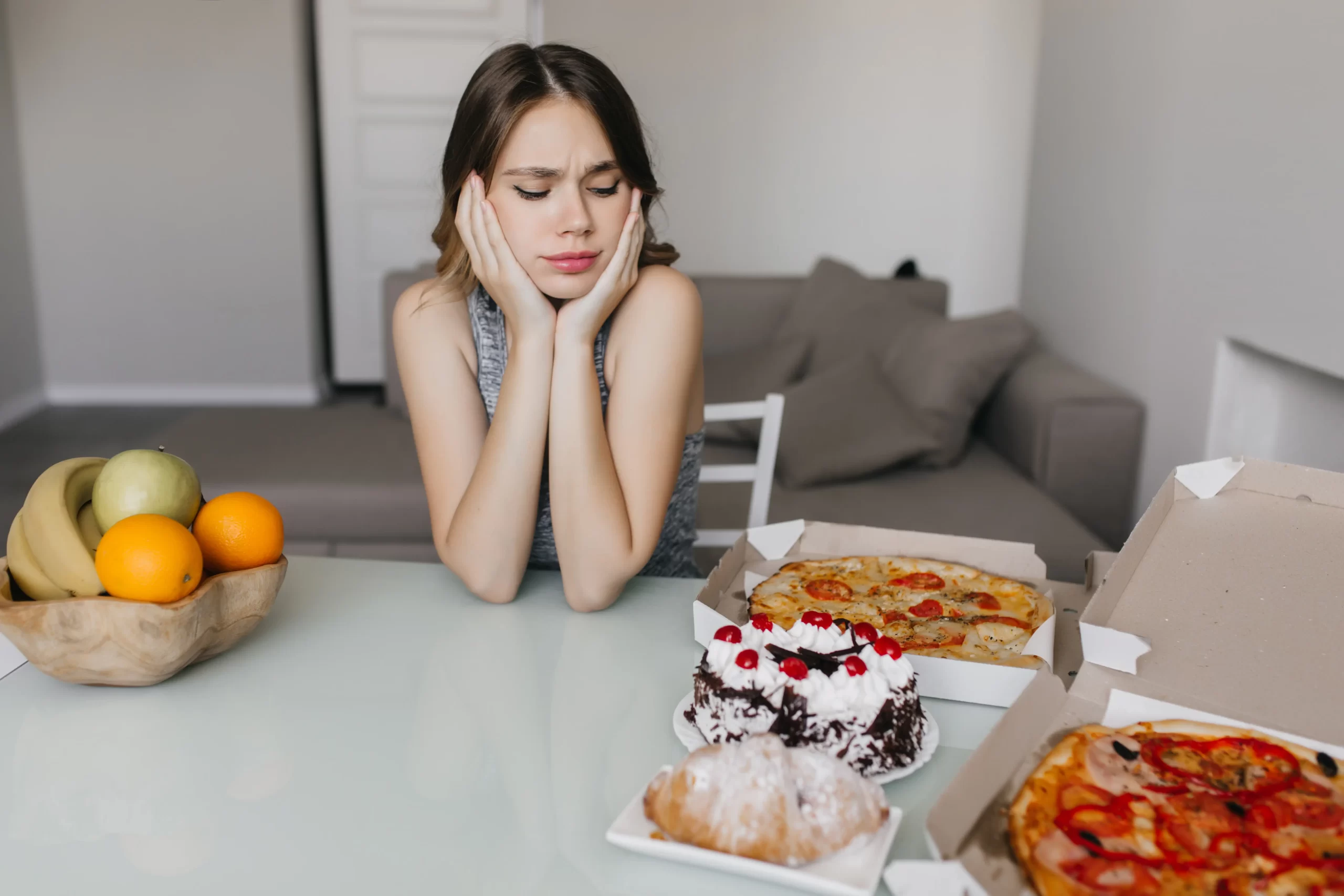 Mulher sentada à mesa com comida à sua frente sem saber o que escolher, indicando um transtorno alimentar.